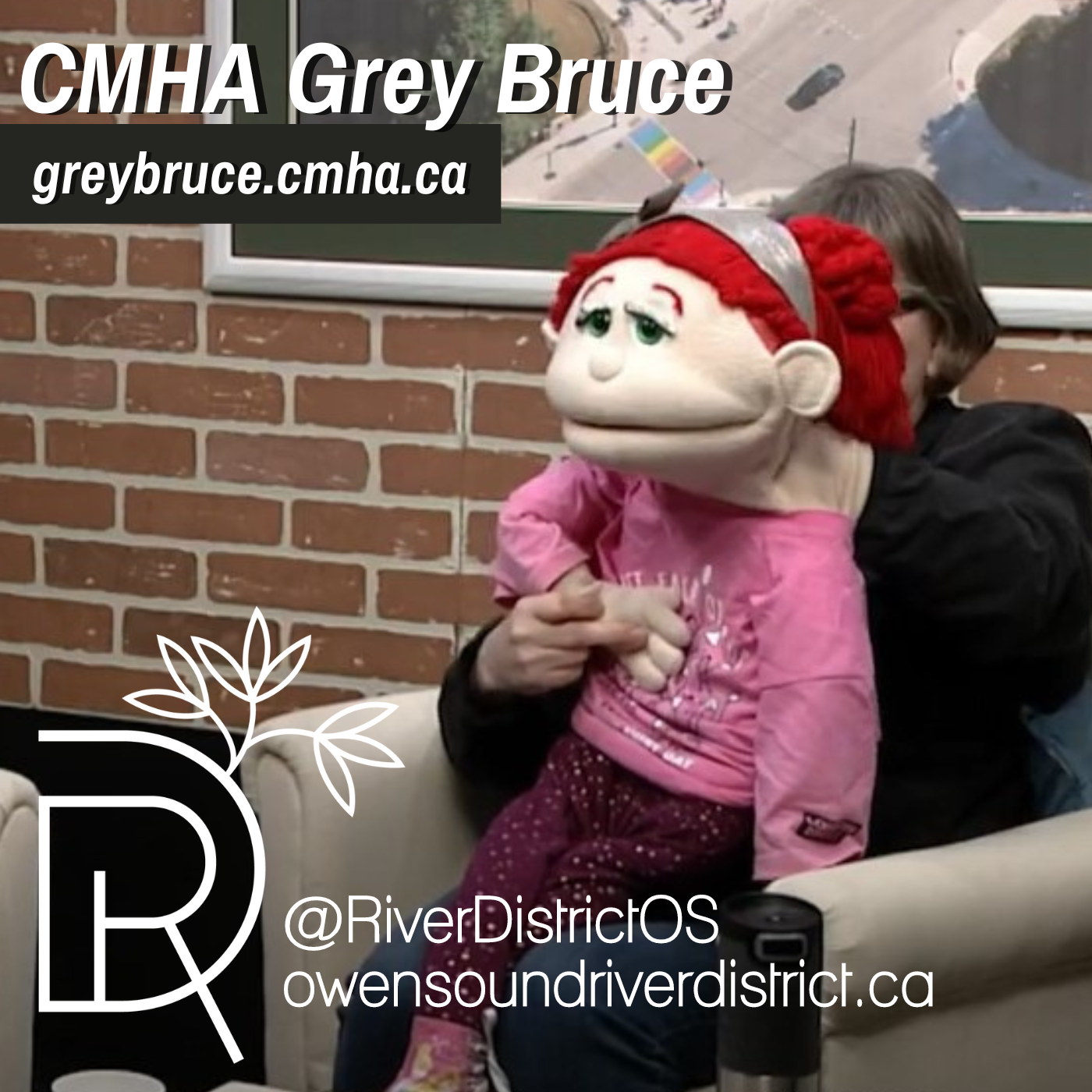 Jackie Ralph with puppet in front of a faux brick wall, large picture frame in white chair