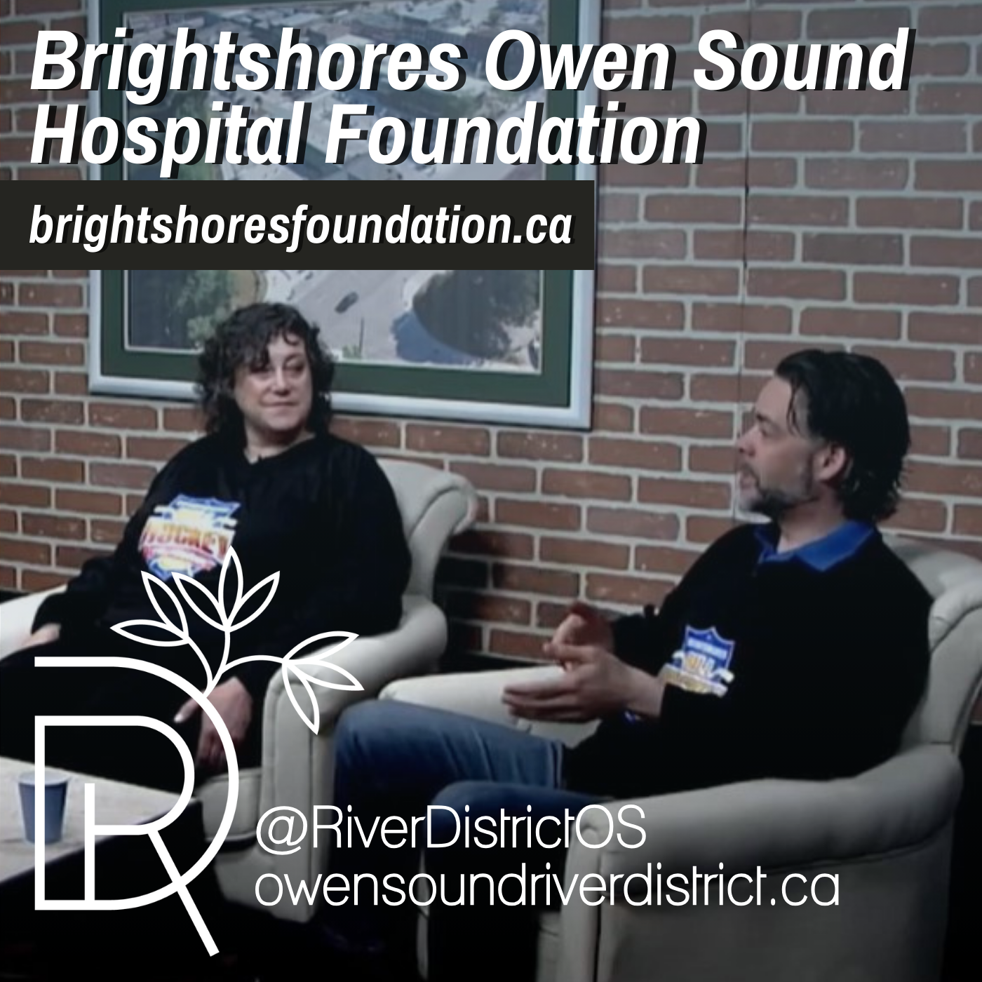 two dark haired guests sitting in white chairs against a faux brick wall and large white framed image of a city