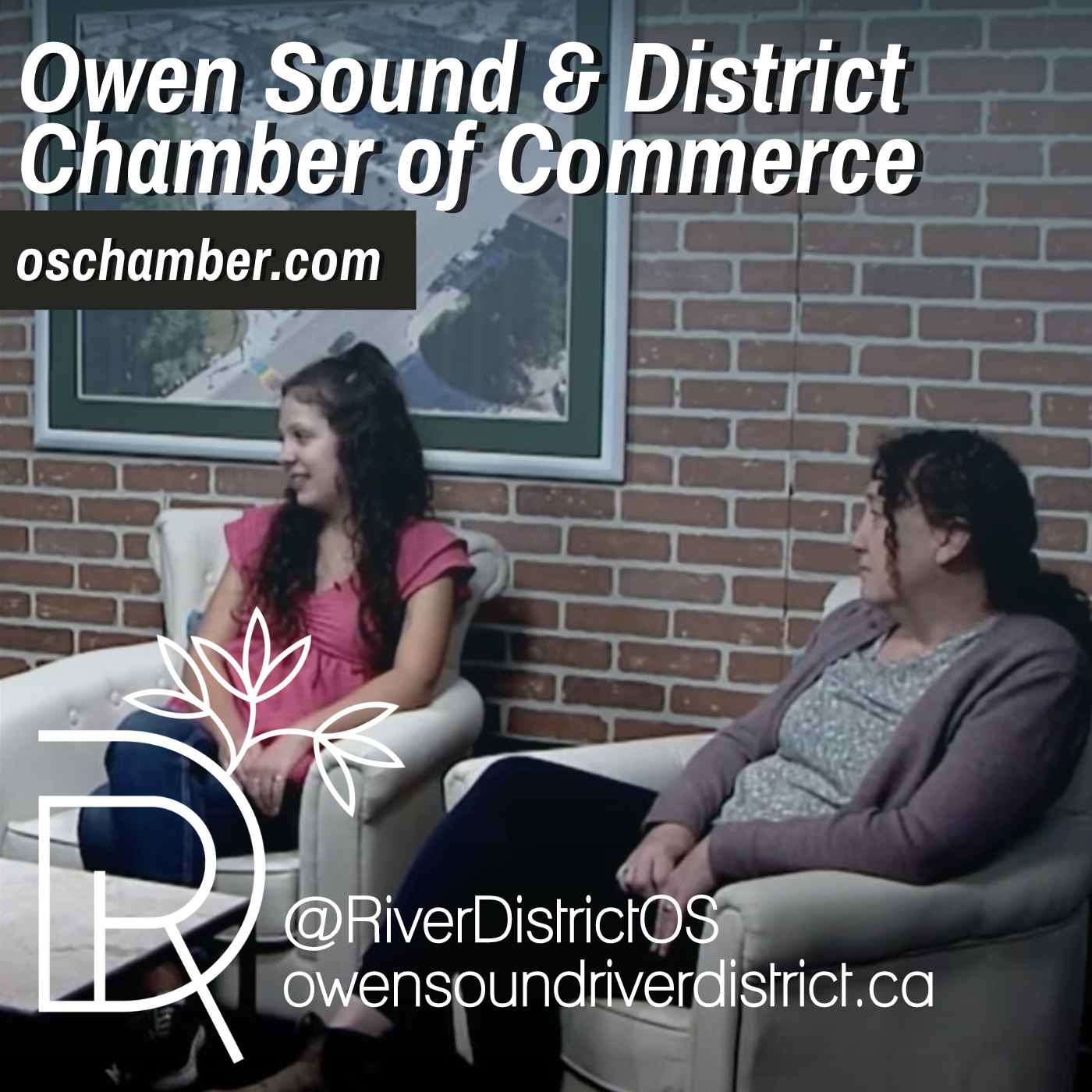 Tiffany James and Savannah Dawson in white chairs against a faux brick wall adorned with a large white frame and areal shot of the City of Owen Sound