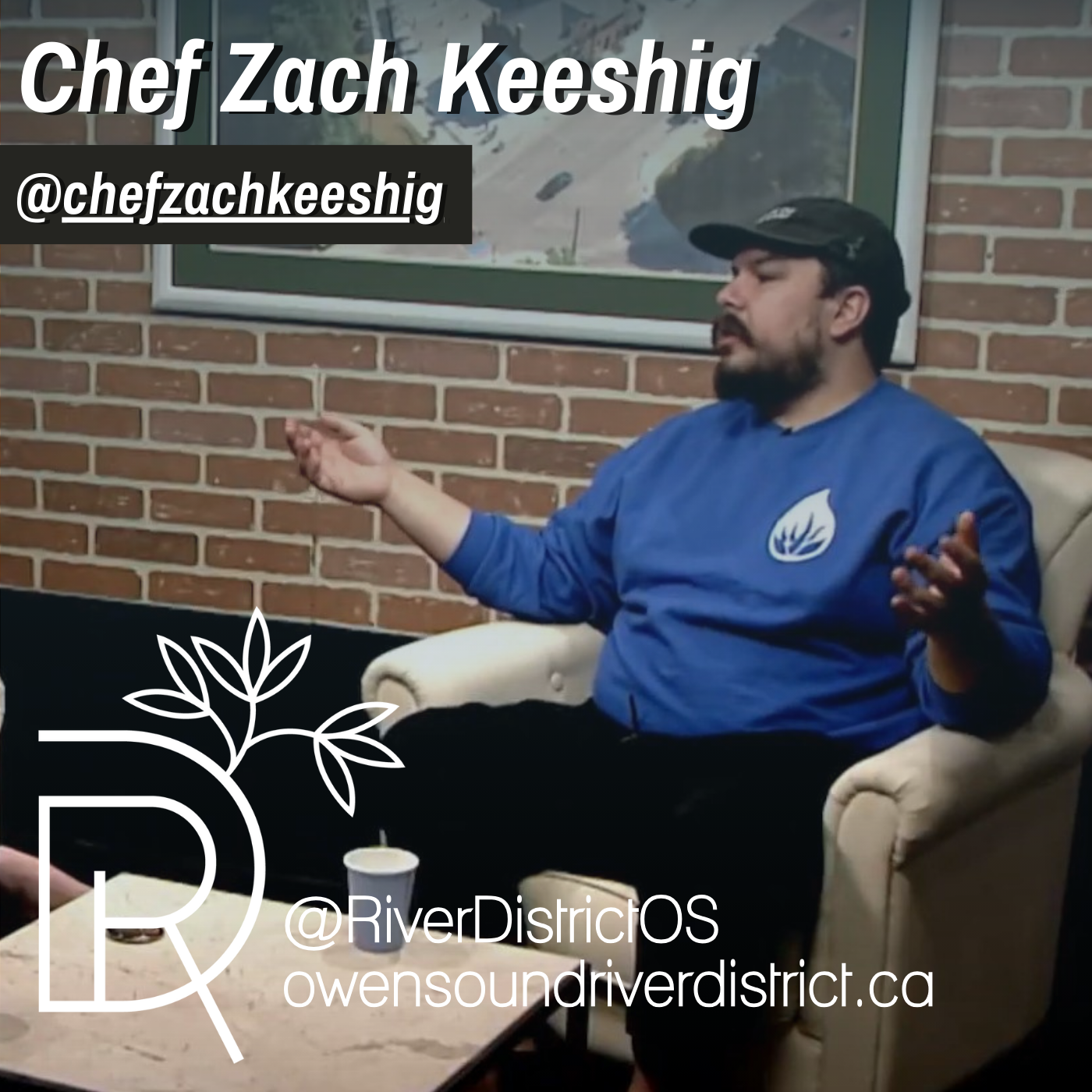 zach keeshig sitting in front of faux brick wall in a white chair wearing a blue long sleeved shirt and black hat