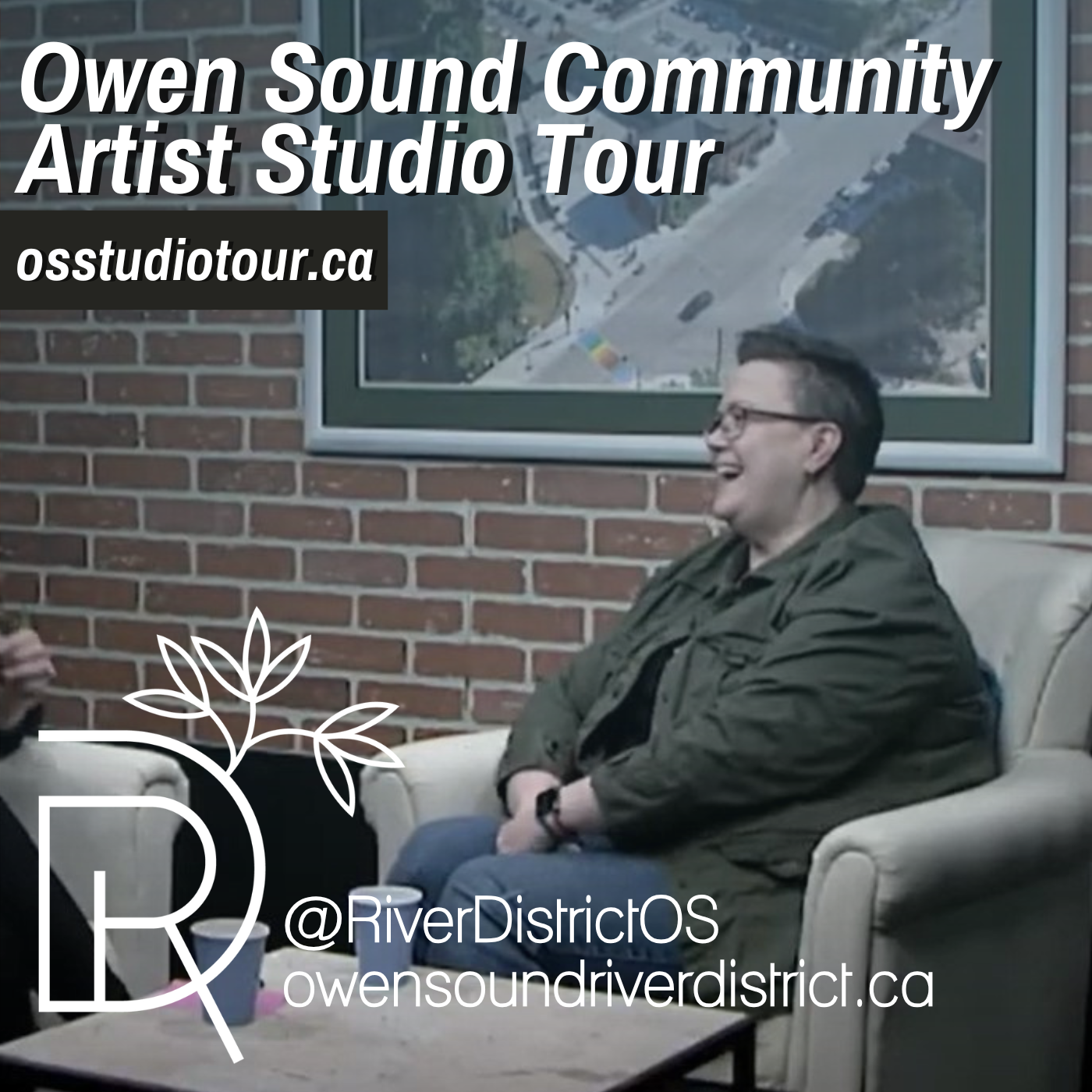 Person with short hair and green jacket in front of a faux brick wall and large painting of an areal shot of a city scape